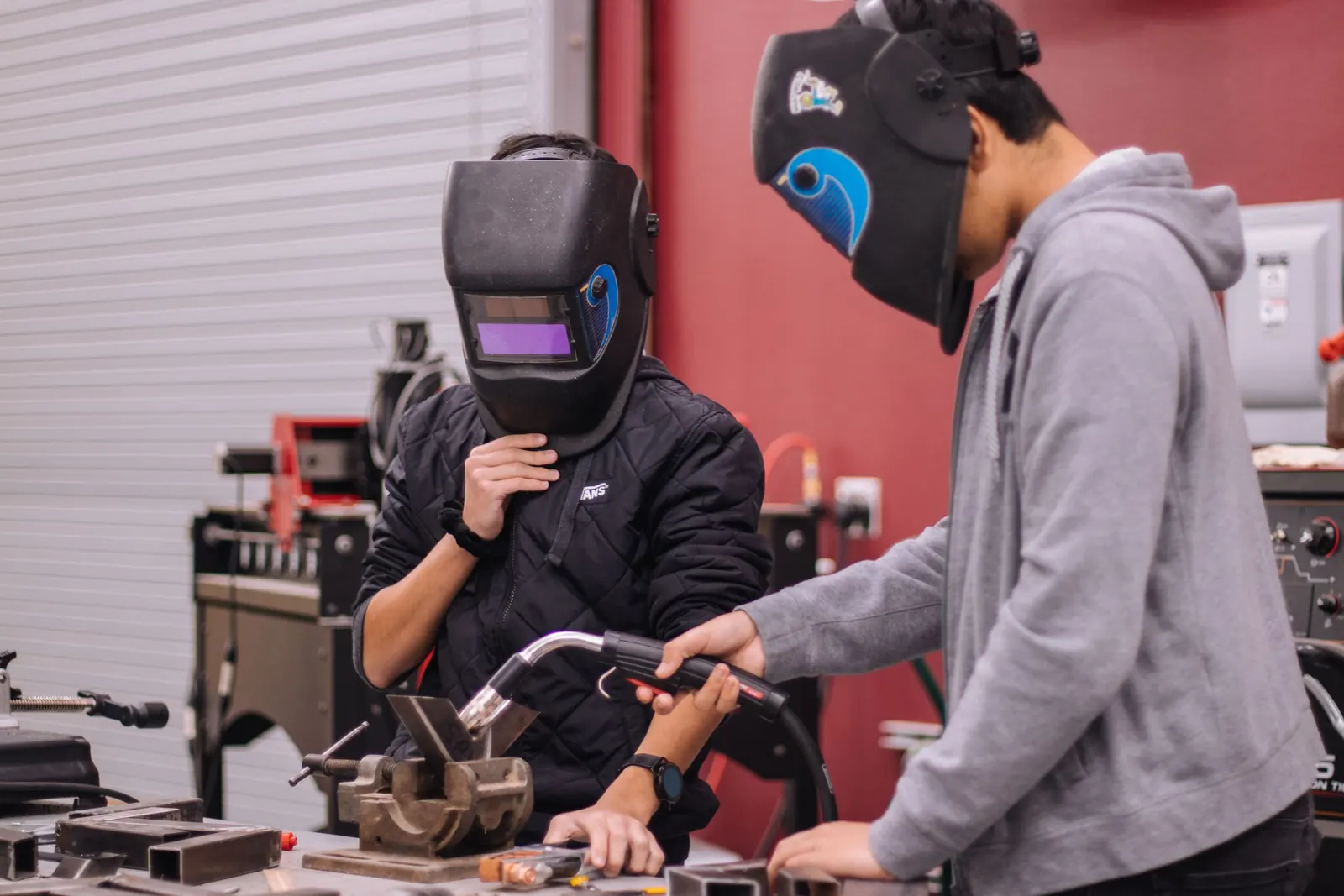 Two students learning to weld at a workbench in a trade-school workshop